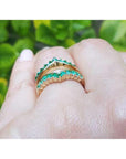 A yellow gold emerald ring guard on a hand against a blurred green leafy background,
