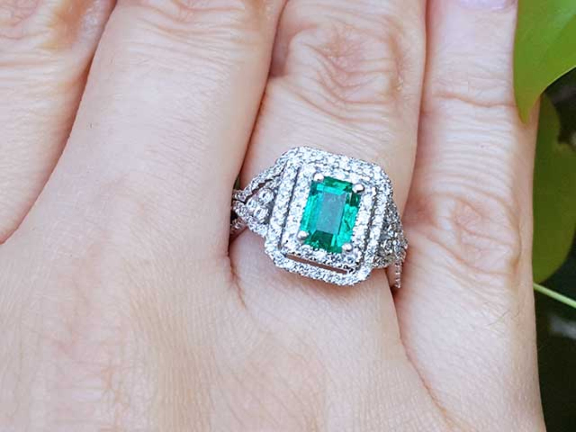 Emerald ring with double halo of diamonds on a finger.