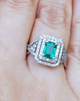 Emerald ring with double halo of diamonds on a finger.