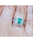 Emerald ring with double halo of diamonds on a finger.