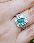 Emerald ring with double halo diamond on a hand against a natural background.