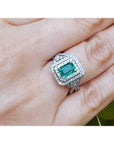 Emerald ring with double halo diamond on a hand against a natural background.