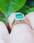 Emerald halo diamond ring underside view on a finger over green leaves background.