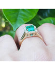 Emerald halo diamond ring underside view on a finger over green leaves background.