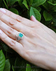 Hand wearing a real Colombian emerald engagement ring against a leafy background.