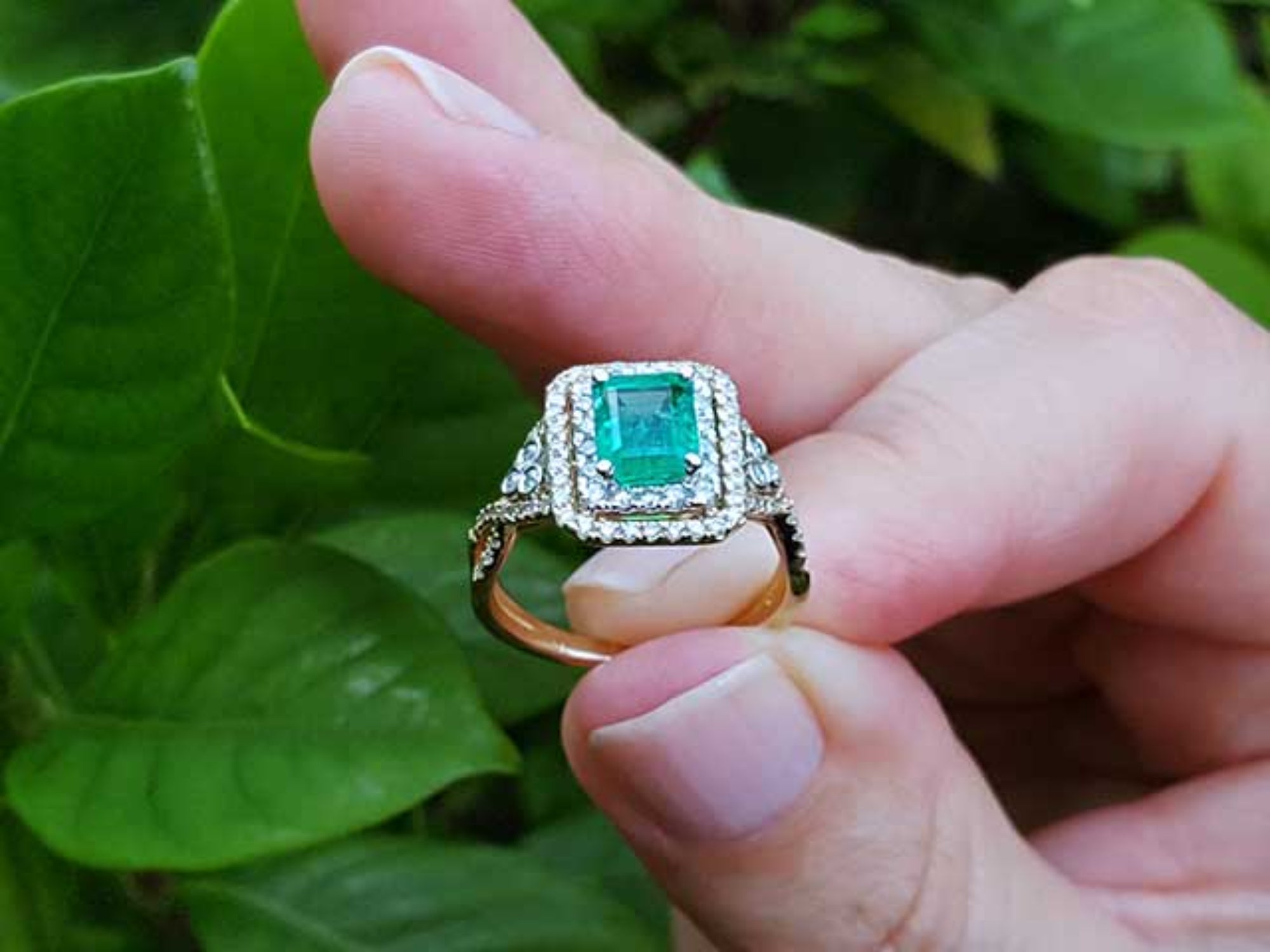 Ring with a natural colombian emerald held between fingers against a natural background.