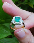 Ring with a natural colombian emerald held between fingers against a natural background.