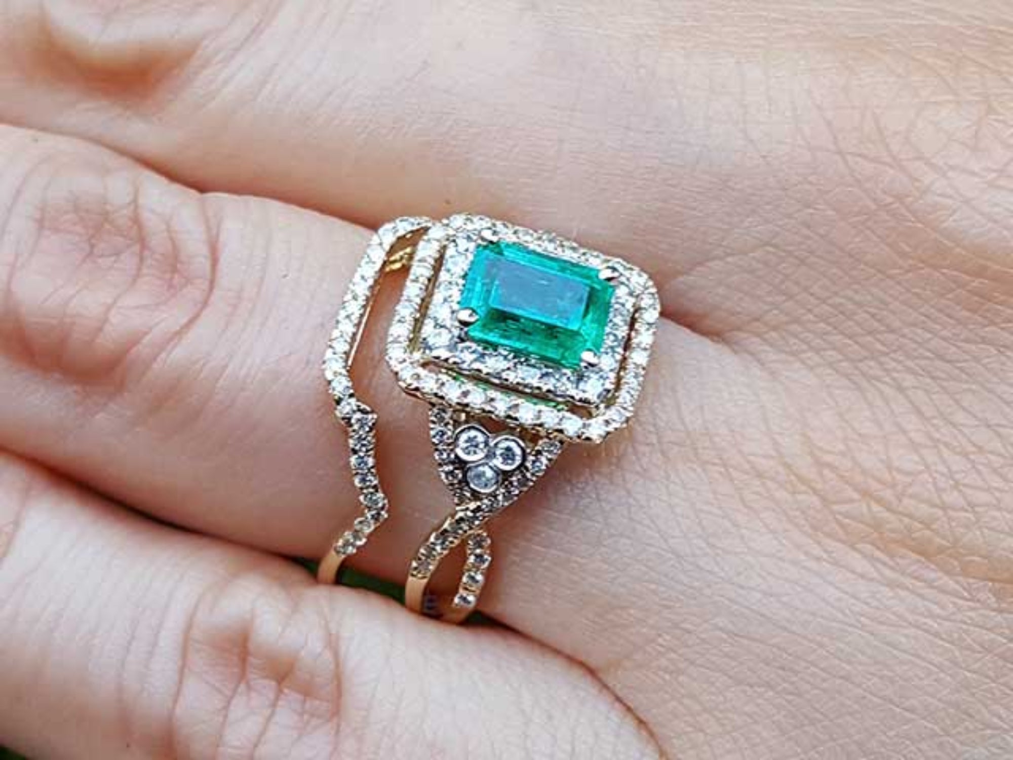 Gold ring with a colombian emerald surrounded by a double halo diamond on a hand.
