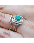 1.31 ct. emerald-cut emerald ring with double diamond halo and matching 14K yellow gold band on a finger.