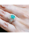 Emerald-cut emerald ring with double diamond halo and matching band in 14K yellow gold on a hand.