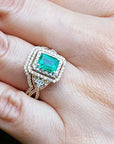 Ring with an emerald-cut emerald within a double halo diamond on a hand.