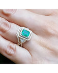 Emerald-cut emerald ring with double diamond halo and matching band in 14K yellow gold on a hand.
