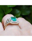 14K yellow gold emerald-cut emerald ring with double diamond halo and matching band on a finger.