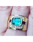 A 18k yellow gold natural emerald ring bezel set with side accent diamonds on a finger.