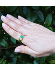 Hand wearing a yellow gold genuine emerald men's ring against a leafy background.
