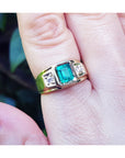 Gold ring for man with a natural colombian emerald on a finger against a blurred natural background.