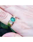 A yellow gold emerald ring for men on a finger against a blurred natural background.