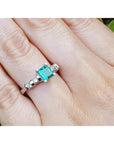 14K white gold ring with a square emerald cut Colombian emerald and sparkling side diamonds on a hand.