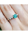 14K white gold ring with a square emerald cut Colombian emerald and side accent diamonds on a hand.