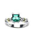 Topside profile view of an emerald and diamonds ring on a white background.