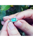 1.21 ct. emerald-cut emerald ring with natural diamonds set in 14K white gold, held by hands.