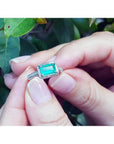 1.21 ct. emerald-cut emerald ring with natural diamonds set in 14K white gold, held by hands.