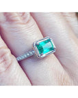 1.21 ct. emerald-cut emerald ring with natural diamonds set in 14K white gold on a finger.