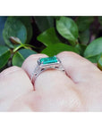 1.21 ct emerald-cut emerald ring with natural diamonds in 14K white gold on a finger.