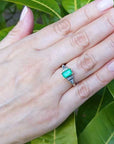 Hand wearing a natural emerald ring with leaves in the background.