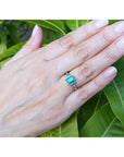 Hand wearing a natural emerald ring with leaves in the background.