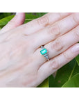 Platinum and 18K yellow gold emerald ring with natural round and trillion-cut diamond accents on a hand.
