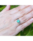 Platinum and 18K yellow gold emerald ring with natural round and trillion-cut diamond accents on a hand.