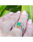 1.21 ct. emerald ring with 18K yellow gold setting, platinum band, and diamond accents on a hand.