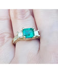 This is a women's emerald ring with princess cut side diamonds and is made of 18k yellow gold.
