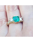 This is a women's emerald ring with princess cut side diamonds and is made of 18k yellow gold.