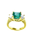 A 18k yellow gold emerald ring with side princess cut diamonds, on a white background.