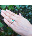 Yellow gold 18K ring with emerald and princess cut side diamonds on a hand.