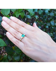Yellow gold 18K ring with emerald and princess cut side diamonds on a hand.