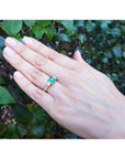Yellow gold 18K ring with emerald and princess cut side diamonds on a hand.