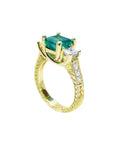 A half side profile of an emerald ring with side princess cut diamonds in 18k yellow gold.
