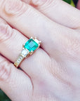 A Mother's Day gift emerald and side princess cut diamonds ring on a person's finger.