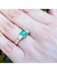 Emerald and princess cut side diamond ring in 18K yellow gold with antique decor on a hand.