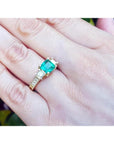 Emerald and princess cut side diamond ring in 18K yellow gold with antique decor on a hand.