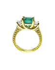 A lateral profile view including gallery of an emerald ring with side princess cut diamonds in 18k yellow gold.