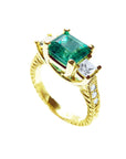 An emerald ring with side princess cut diamonds on a white background.