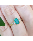 A natural colombian emerald and side baguette diamonds ring for women on a finger.