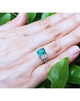 1.88 carat emerald ring with side emerald-cut and round diamonds in 18k white gold on a hand.