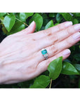 Emerald ring with side emerald-cut and round diamonds in 18k white gold on a hand.