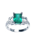 A tree stone emerald engagement ring with side emerald-cut natural side diamonds made of 18k white gold.