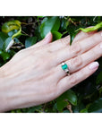 18k white gold three stone ring with a 1.38 ct emerald and two princess cut diamonds on a hand.
